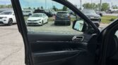 Open car door on the left, looking out at a parking lot with several vehicles including a white sedan in front and a dark SUV in the middle; interior door panel visible.
