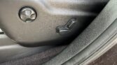 Side view of a car driver's seat with manual adjustment lever and a round knob on a black plastic panel near the seat base.