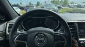 Front-seat view inside a Jeep: steering wheel with logo, dashboard, and a crowded parking lot visible through the windshield