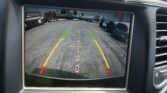 Rearview/backup camera display showing parking guidelines with green, yellow, red lines and the message 'Check Entire Surroundings' (car interior shown).