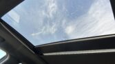 Inside a car looking up at the panoramic sunroof with blue sky and clouds outside.