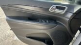 Interior view of a car door panel featuring a chrome door handle and window controls, with the outside parking lot visible through the window