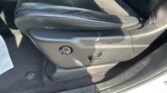 Black leather car seat edge with visible seat adjustment knob and lever on the side, inside a vehicle.