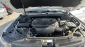 Open car hood revealing the engine bay with a V6 engine cover and front grille visible behind the windshield wipers in a parking lot.