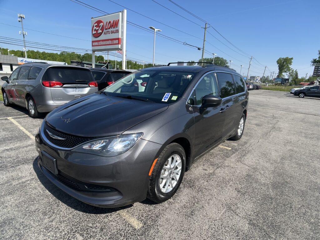 Dark gray SUV in the foreground at a car dealership lot, with a large EZ LOAN Auto Sales sign in the background on a clear day.