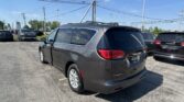 Rear three-quarter view of a gray Chrysler Voyager minivan in a dealership lot, with other cars and a Toyota sign in the background.
