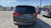 Rear view of a black Chrysler Voyager minivan in a busy parking lot, with other cars and power lines overhead under a blue sky.
