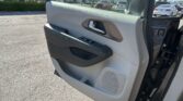 Interior view of a car door panel with a chrome handle and window controls; a dealership parking lot is visible outside the window.