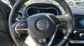 Close-up of a Jeep steering wheel with center logo, surrounding controls, and a partial dashboard display behind it in a car interior