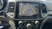 Infotainment screen showing the car's rearview camera with green/yellow/red guiding lines in a parking lot.
