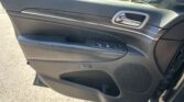 Interior of a car door panel with a chrome door handle, wood trim, black leather, window controls at the armrest, and a speaker grille nearby