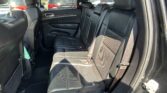 Rear passenger seats in a black leather SUV with seat belts fastened and sunlit windows.
