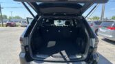 Open SUV hatch revealing spacious cargo area with third-row seats upright, in a dealership parking lot.