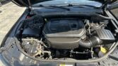 Under-hood view of a vehicle's engine bay with a prominent V6 cover and various hoses and components visible.