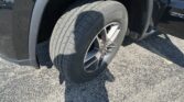 Close-up of a car tire and wheel in the front wheel well of a dark SUV on pavement.