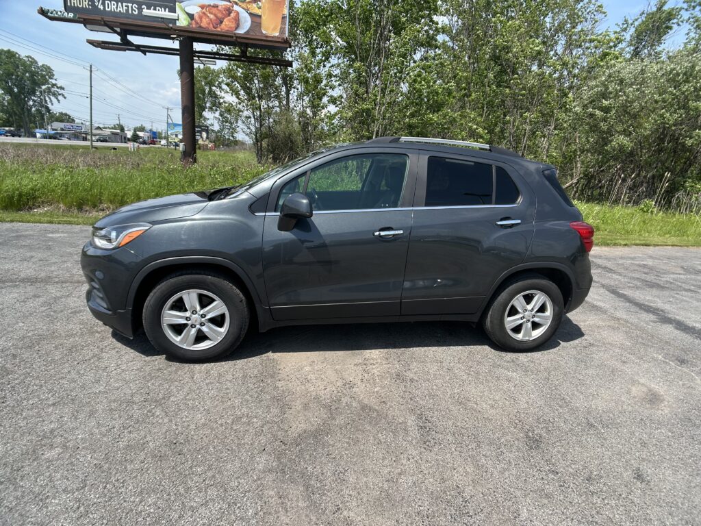 Gray SUV parked on a paved lot with a large billboard and green trees in the background