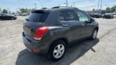 Gray SUV photographed from the rear-right in a busy parking lot with other cars and dealership buildings in the background.