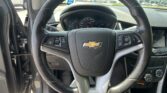 View from the driver's seat showing a Chevrolet steering wheel and instrument cluster, with the door open in a dealership lot outside