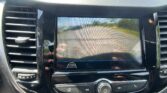 Car dashboard display showing a rearview camera view with orange guide lines over the road behind the vehicle