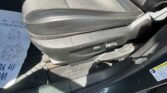 Close-up of a car seat cushion showing black fabric and light brown stitching, with visible edge wear and a side adjustment lever nearby.