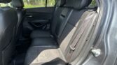 Rear row of a car with black leather seats, headrests, and visible seat belts in the daylight outside the window.