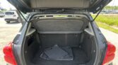 Open hatch of a dark SUV showing the cargo area with a stack of black floor mats and folded rear seats in view. Red tail light edge visible at bottom corner.