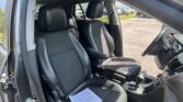 Dark leather car interior with front seats and steering wheel visible; papers lie on the driver's seat as the door is open, outside parking lot visible.
