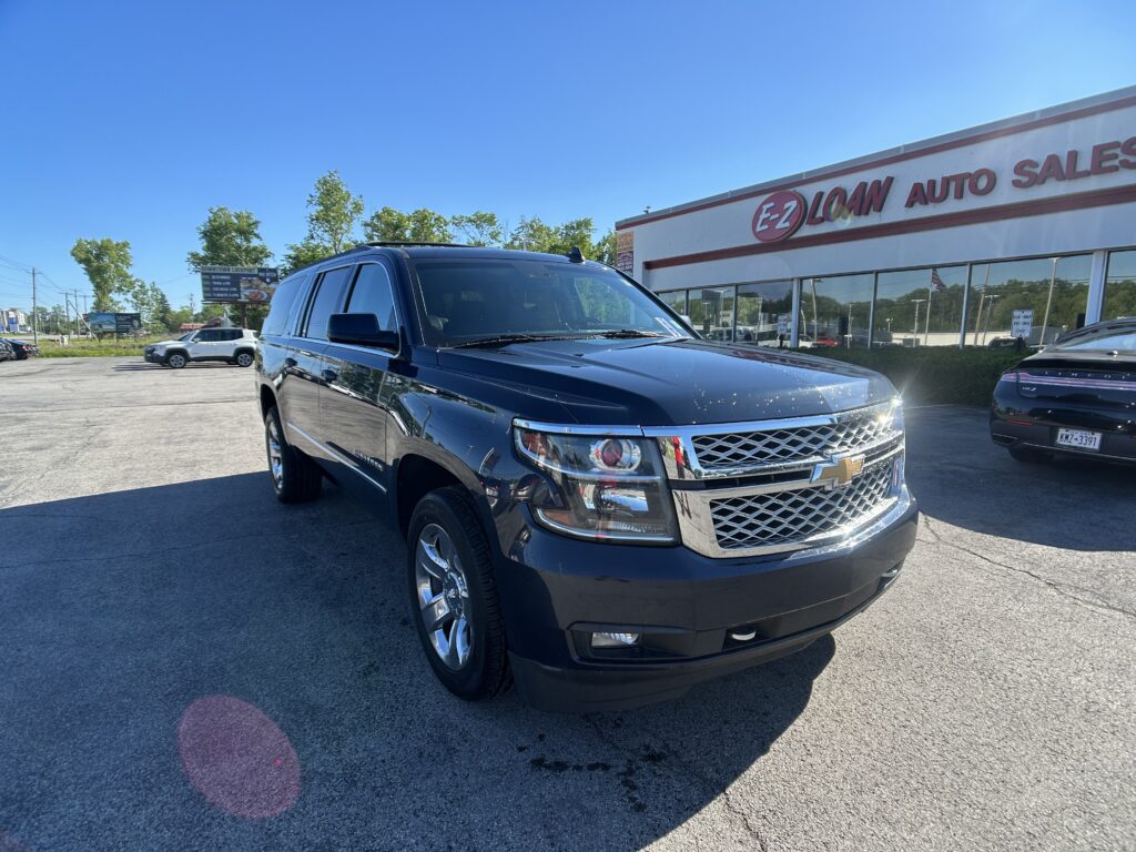 Black SUV in the foreground at a car dealership lot with the EZ Loan Auto Sales storefront in the background on a sunny day.