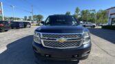 Front view of a dark blue Chevrolet pickup in a dealership lot with other cars and a clear blue sky behind it.
