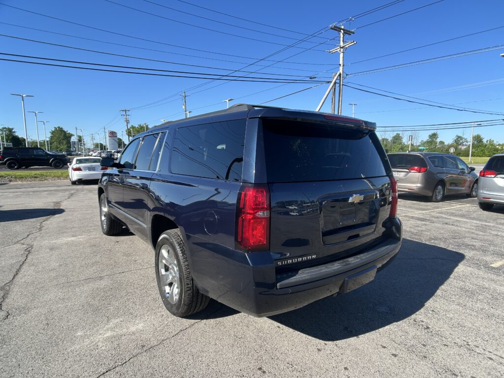 Rear view of a black Chevrolet Suburban in a parking lot under a clear blue sky with power lines overhead.