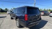 Rear view of a black Chevrolet Suburban in a parking lot under a clear blue sky with power lines overhead.