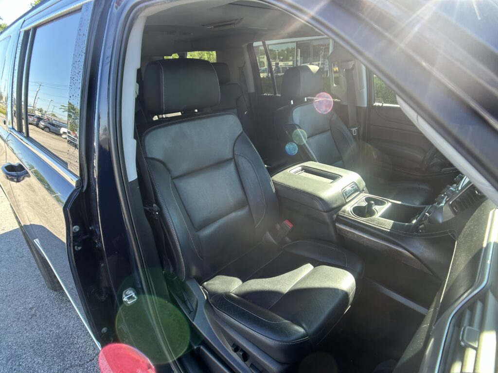 Dark leather SUV interior with front seats and center console, door open on a sunny day, lens flare in the foreground