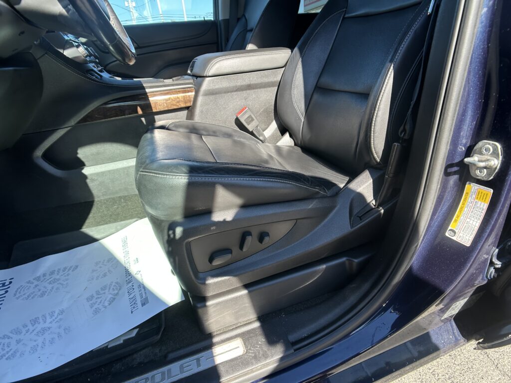 Leather front seat area of a vehicle with a center console, wood trim, and visible seat belt buckle on the passenger side; door frame and exterior visible at right.