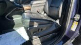 Leather front seat area of a vehicle with a center console, wood trim, and visible seat belt buckle on the passenger side; door frame and exterior visible at right.