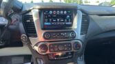 Inside view of a car dashboard showing a center touchscreen with radio controls and climate dials on the console below, and a steering wheel to the left.