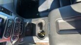 Interior of a car center console: black leather seats, climate control knobs, and a cup holder with a yellow bottle cap in it.
