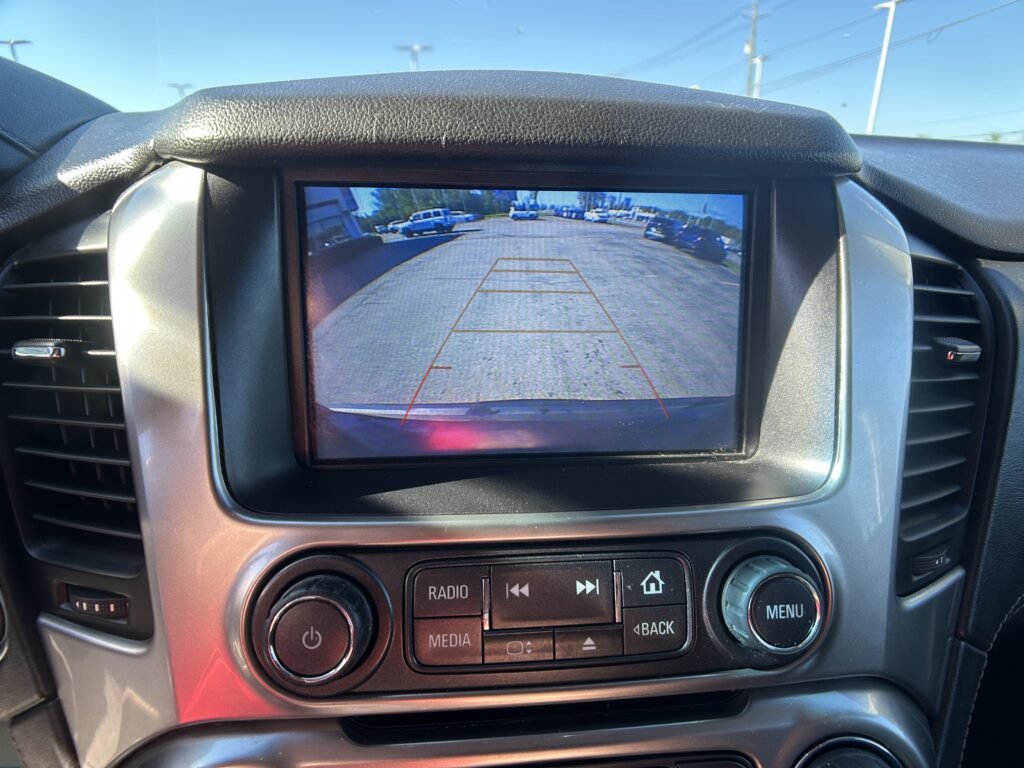 Car’s rearview camera display showing a parking lot with parked cars on both sides and guiding red and orange lines for reversing safety