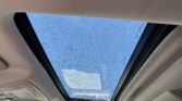 Inside a car looking up at an open panoramic sunroof with raindrops on the glass and blue sky beyond
