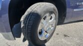Close-up of a blue SUV wheel and tire, showing the tread and chrome rim, with part of the vehicle’s side badge visible (likely 'SUBURBAN').
