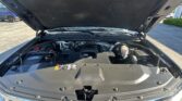 Open hood showing engine bay of a Chevrolet vehicle in a parking lot, with visible engine components and hoses.