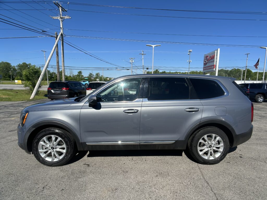 Silver SUV parked in a car dealership lot under a clear blue sky with power lines overhead and a sign in the distance.