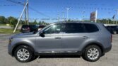 Silver SUV parked in a car dealership lot under a clear blue sky with power lines overhead and a sign in the distance.