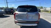 Rear view of a silver Kia Telluride in a dealership parking lot with other cars and power lines overhead.