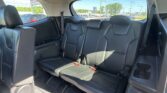 Back seats of a black leather SUV with three seating positions and visible seat belts; showroom lot visible through the rear windows.