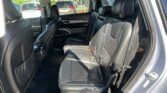 Interior of a black leather SUV showing the back seats with seat belts and headrests, viewed from the open rear door, with a parking lot outside the windows.
