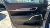 Interior car door panel with silver door handle, window controls, and speaker grille; parking lot visible through window outside