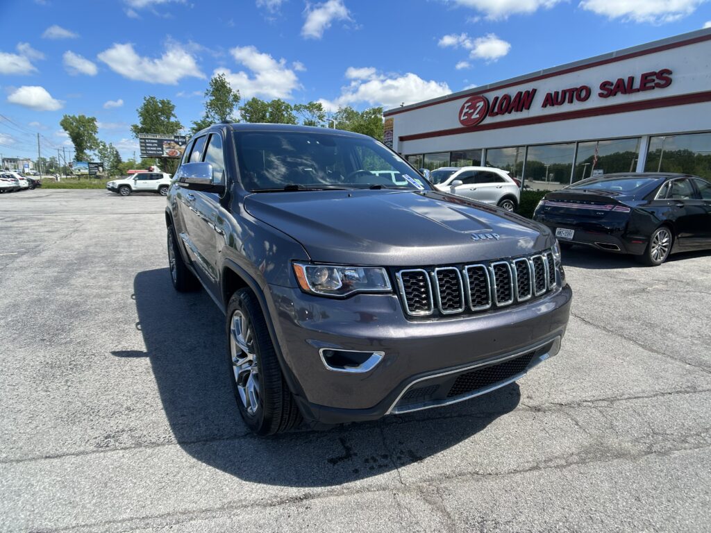 Front-left corner view of a gray Jeep SUV parked at a car dealership lot in front of the EZ Loan Auto Sales storefront.