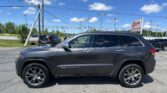 Gray Jeep Grand Cherokee SUV parked in a car dealership lot with an EZ Loan Auto Sales sign in the background and power lines overhead under a blue sky.