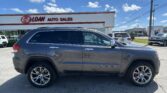 Gray Jeep Grand Cherokee in foreground at EZ LOAN Auto Sales lot with dealership building and blue sky in the background