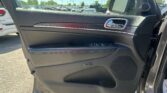 Open car door interior with black panel and chrome handle; parking lot visible outside on a sunny day